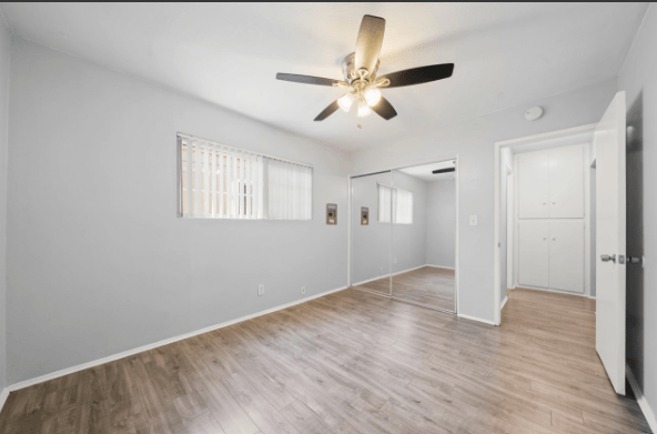 A room with a ceiling fan and wooden flooring.